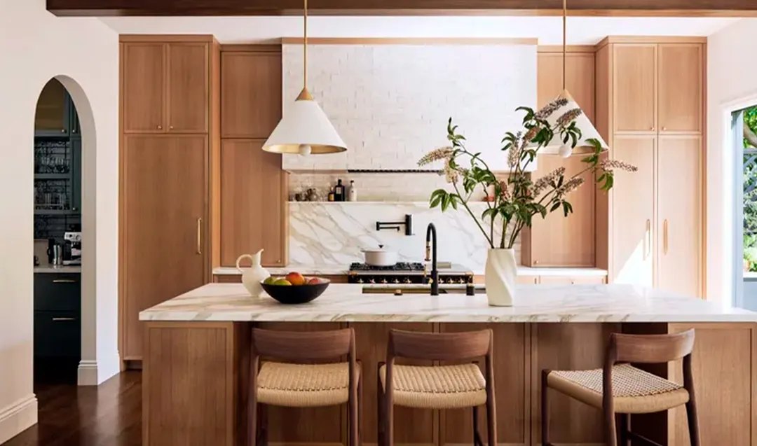 La combinación de suelo de madera oscura, armarios de madera media y encimeras de piedra blanca crea en esta cocina una composición elegante y equilibrada.
