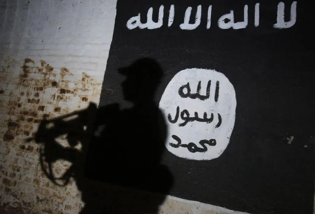 La sombra de un combatiente armado se proyecta sobre una pared pintada con la bandera del Estado Islámico (EI).