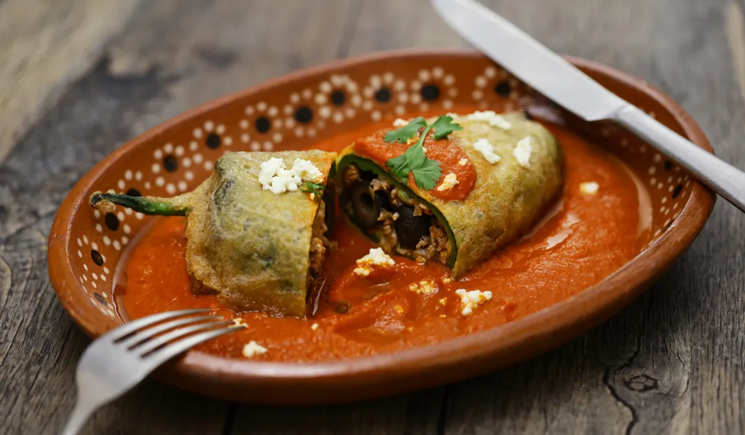La receta de chiles rellenos de picadillo combina ingredientes prehispánicos, como el chile poblano, con influencias españolas como las pasas y almendras, creando un platillo mestizo muy representativo de México.