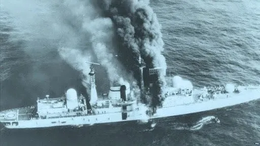 El destructor clase 42 HMS Sheffield minutos después del impacto. Puede verse a su tripulación reunida en proa y en popa y a un bote neumático a estribor. 